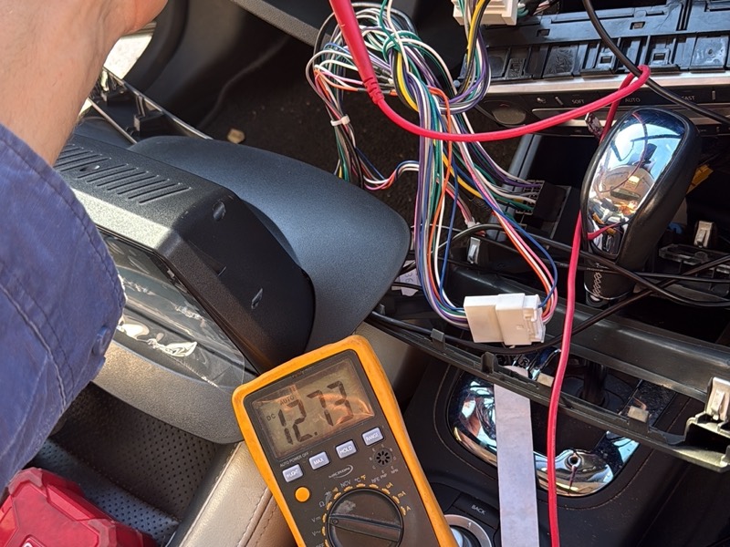 Automotive accessory wiring being tested with a multimeter during installation